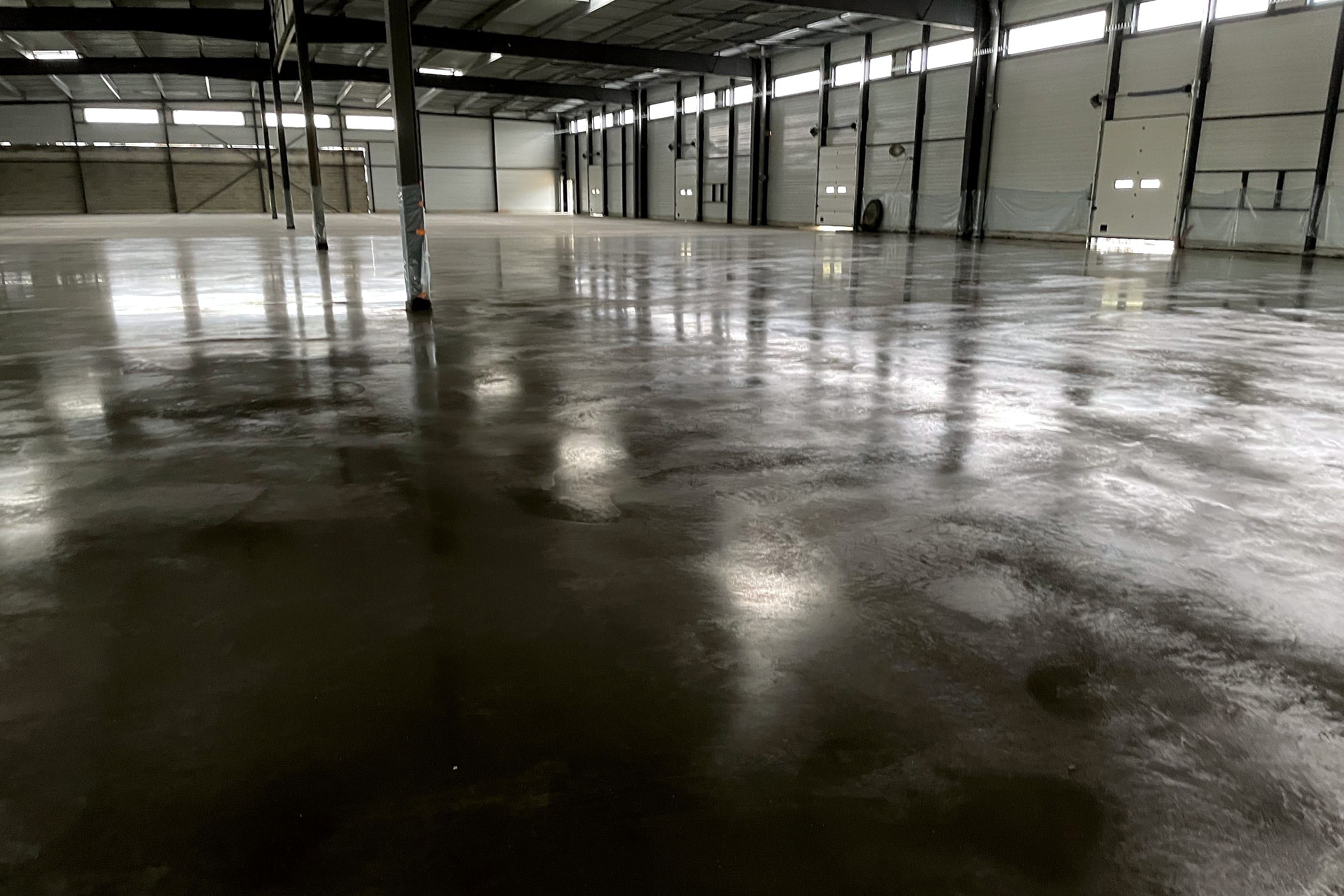 Dallage industriel fraîchement lissé, surface fermée et brillante, dans une halle logistique